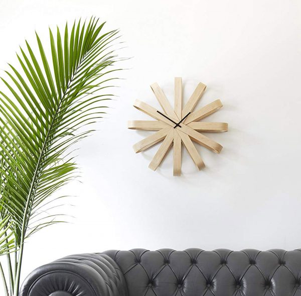 đồng hồ treo tường bằng gỗ ấn tượng, ph&iacute;a dưới l&agrave; ghế sofa da m&agrave;u đen, cạnh đ&oacute; l&agrave; chậu cảnh xanh tốt