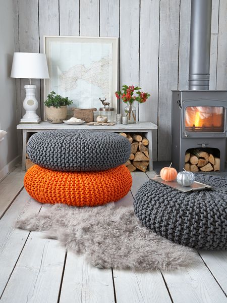 hình ảnh cận cảnh những chiếc đệm ngồi màu cam, xám đặt trên sàn nhà, cạnh đó là bàn gỗ để đèn bàn, khung tranh