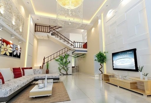 h&igrave;nh ảnh ph&ograve;ng kh&aacute;ch nh&agrave; ống với trần caot ho&aacute;ng, tường sơn m&agrave;u trắng, sofa trắng, tranh hoa treo tường, đ&egrave;n ch&ugrave;m lớn, cạnh đ&oacute; l&agrave; cầu thang l&ecirc;n tầng tr&ecirc;n