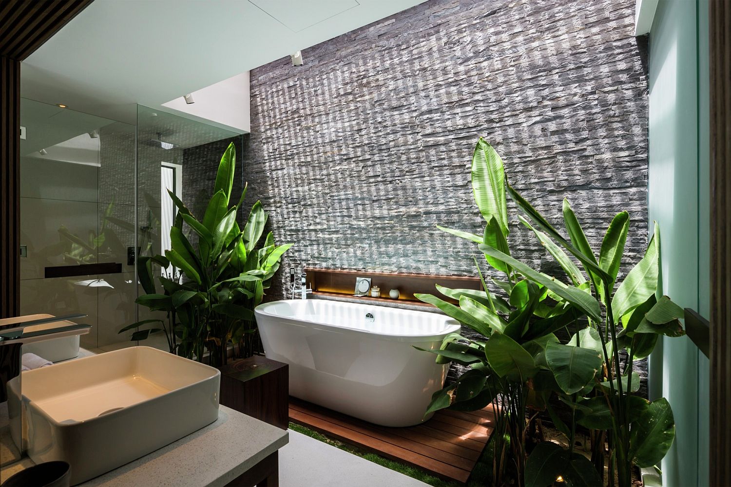 ph&ograve;ng tắm với bồn tắm sứ m&agrave;u trắng, xung quanh l&agrave; c&aacute;c loại c&acirc;y cảnh nhiệt đới xanh tốt