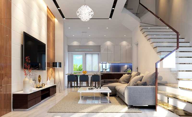 hình ảnh phòng khách nhà ống với bộ ghế sofa màu ghi xám, tủ kệ tivi đối diện, đèn chùm màu trắng, bên trong là khu bếp nấu và phòng ăn, cạnh đó là cầu thang lên tầng trên