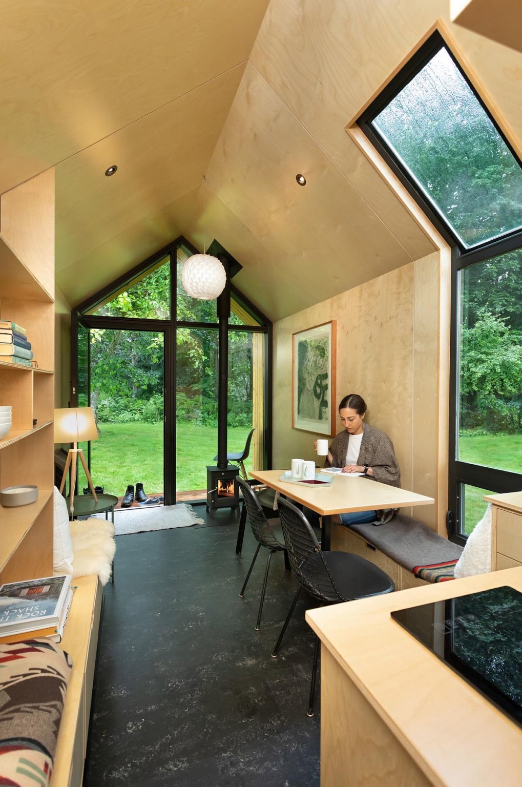 h&igrave;nh ảnh kh&ocirc;ng gian b&ecirc;n trong nh&agrave; cabin với nội thất gỗ tuyết t&ugrave;ng m&agrave;u s&aacute;ng, người phụ nữ uống c&agrave; ph&ecirc;, l&agrave;m việc