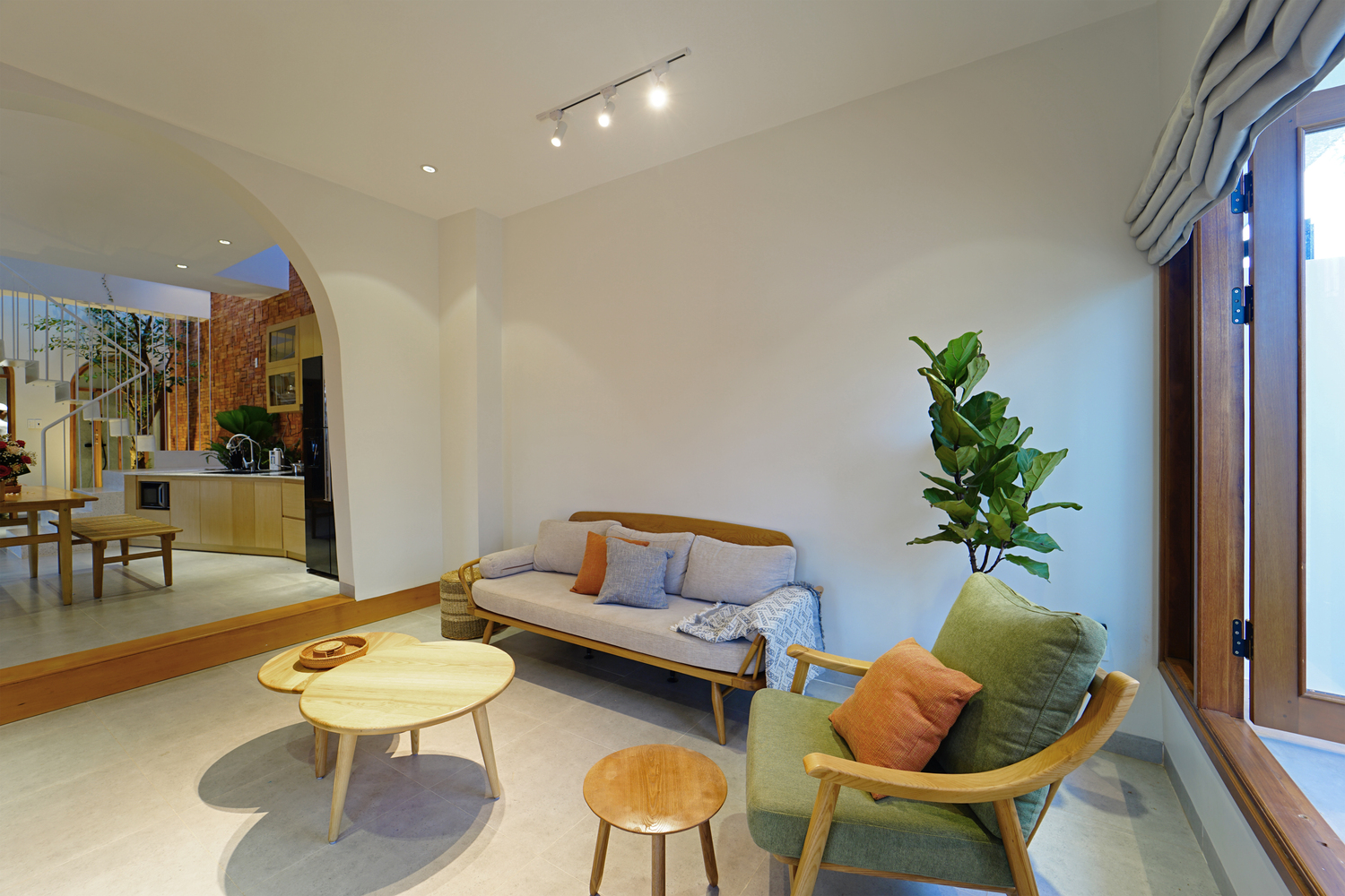 h&igrave;nh ảnh ph&ograve;ng kh&aacute;ch nh&agrave; phố với tường sơn trắng, b&agrave;n tr&agrave; gỗ đ&ocirc;i h&igrave;nh tr&ograve;n, sofa gỗ l&oacute;t đệm m&agrave;u x&aacute;m v&agrave; xanh n&otilde;n chuối