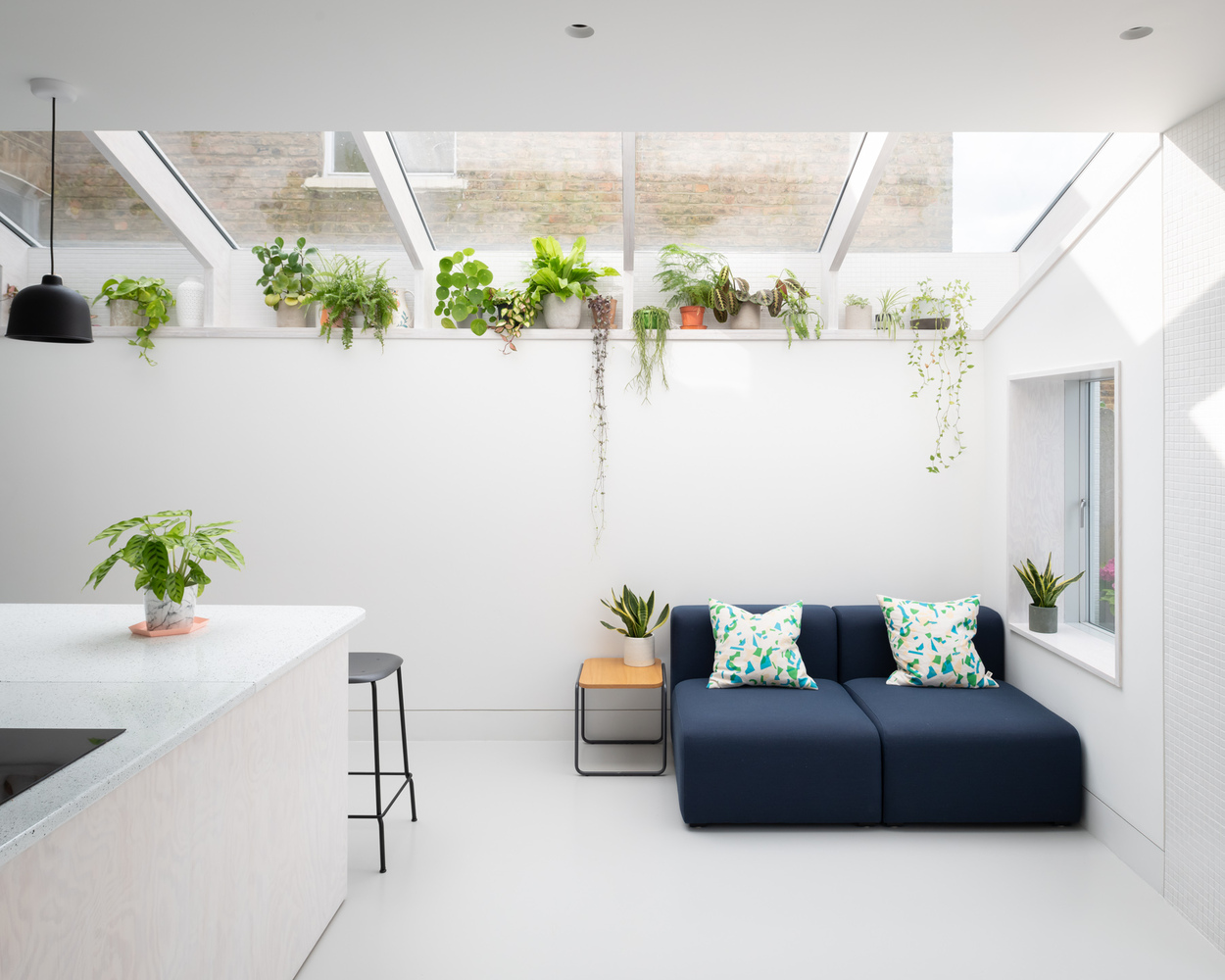 Ph&ograve;ng kh&aacute;ch nhỏ được đ&oacute;ng khung gọn g&agrave;ng bởi ghế sofa xanh than, b&agrave;n phụ, bộ đ&ocirc;i gối tựa hoa văn m&agrave;u xanh ngọc, c&ugrave;ng chậu cảnh đối xứng hai b&ecirc;n.