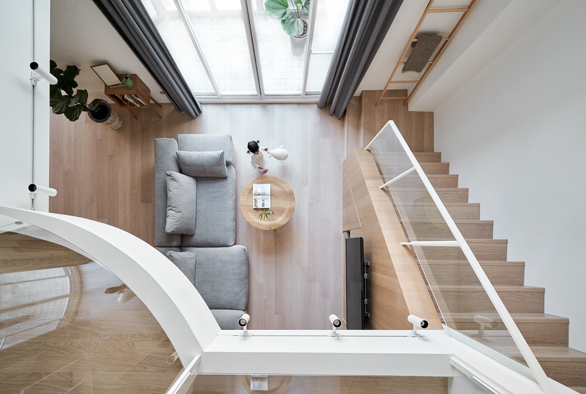 toàn cảnh phòng khách nhìn từ trên xuống với sofa xám, bàn trà gỗ tròn, cửa kính, rèm xám, cây xanh trang trí