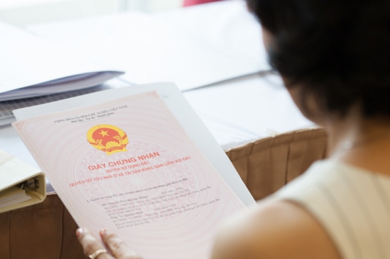 mộ người phụ nữ đang cầm cuốn sổ hồng, tr&ecirc;n b&agrave;n l&agrave; nhiều giấy tờ kh&aacute;c