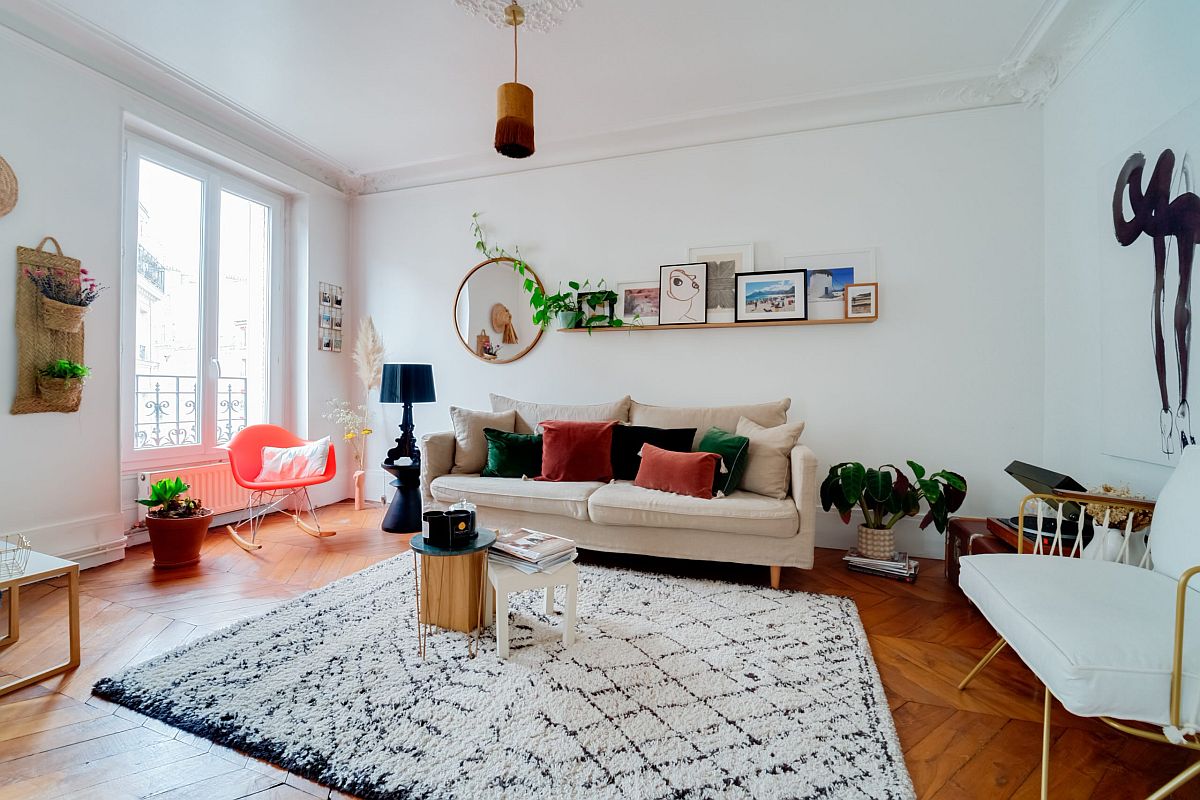 hình ảnh phòng khách rộng rãi với màu trắng chủ đạo, gối tựa sofa màu sắc, thảm trải họa tiết hình học màu đen trắng, cây xanh trang trí, gương tròn treo tường, cửa sổ kính