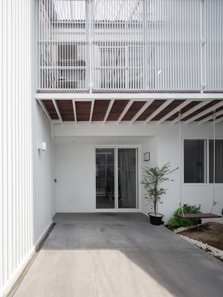 Lối vào nhà lát bê tông xám mộc mạc, hài hòa với sơn tường màu trắng và chất liệu kính trong suốt của hệ cửa chính, cửa sổ.