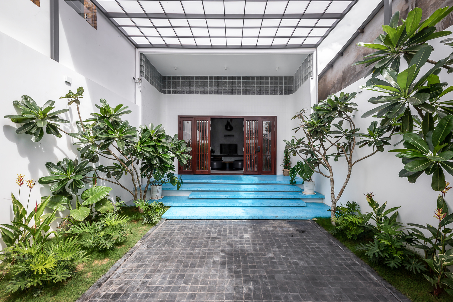 Sân trước nhà ống trồng nhiều cây xanh hình ảnh sân trước nhà ống lát gạch xám, trồng cây xanh hai bên, bậc tam cấp màu xanh lam