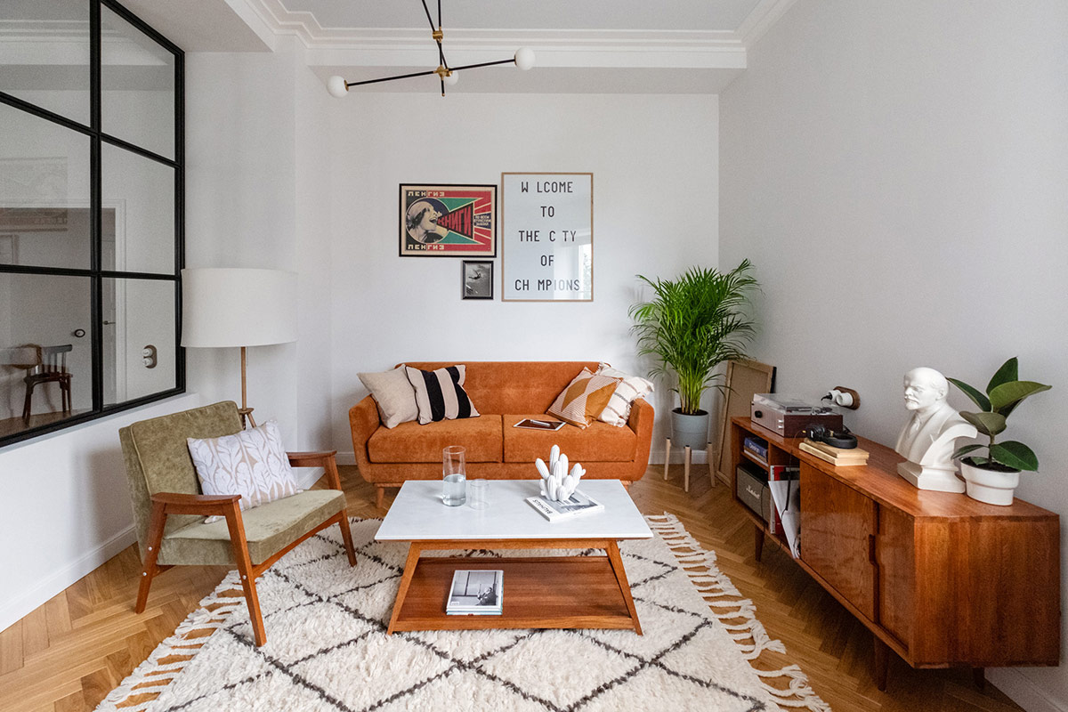 Trong ph&ograve;ng kh&aacute;ch căn hộ 74m2, đồ nội thất m&agrave;u n&acirc;u l&agrave;m ấm kh&ocirc;ng gian sống phong c&aacute;ch Mid-Century t&ocirc;ng trắng chủ đạo. Thảm trải c&oacute; tua rua tạo điểm nhấn sinh động.