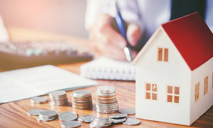 hình ảnh mô hình ngôi nhà với mái ngói đỏ, các cọc tiền xu màu trắng để trên bàn