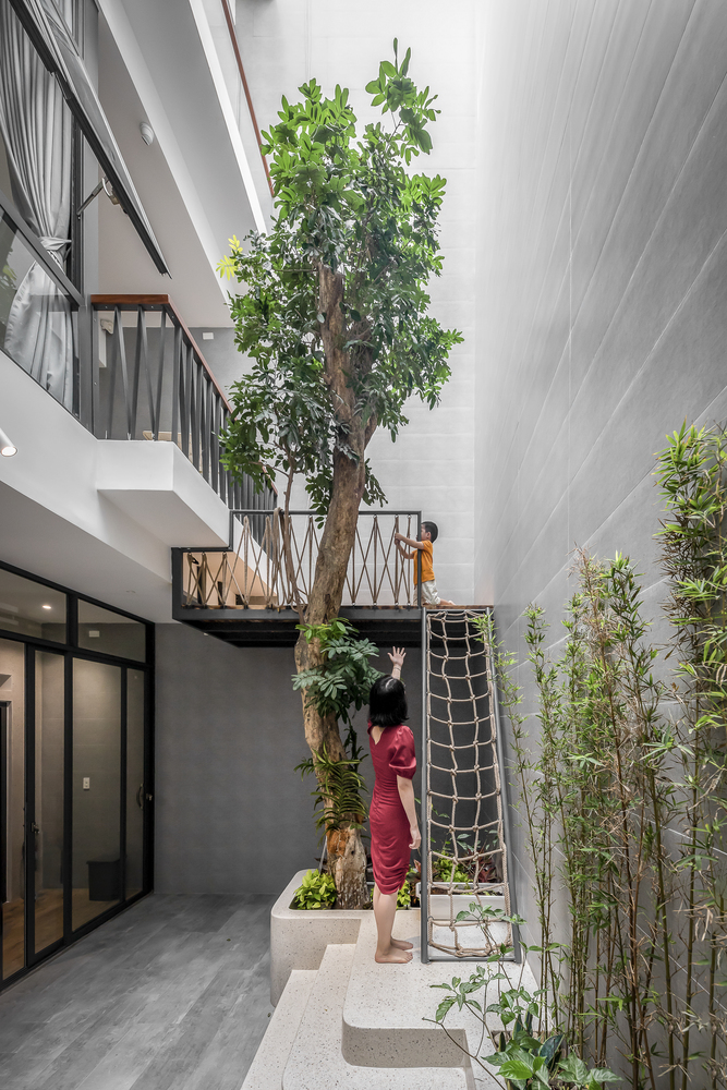 hình ảnh người mẹ mặc váy đỏ vui đùa với con trai ở khu vực giếng trời, cây xanh thoáng sáng