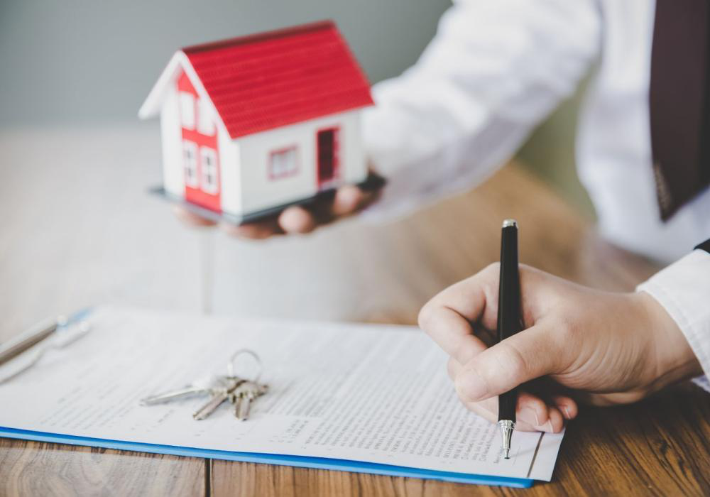 hình ảnh cận cảnh mô hình ngôi nhà cấp 4 mái ngói đỏ, một người đang ký kết hợp đồng