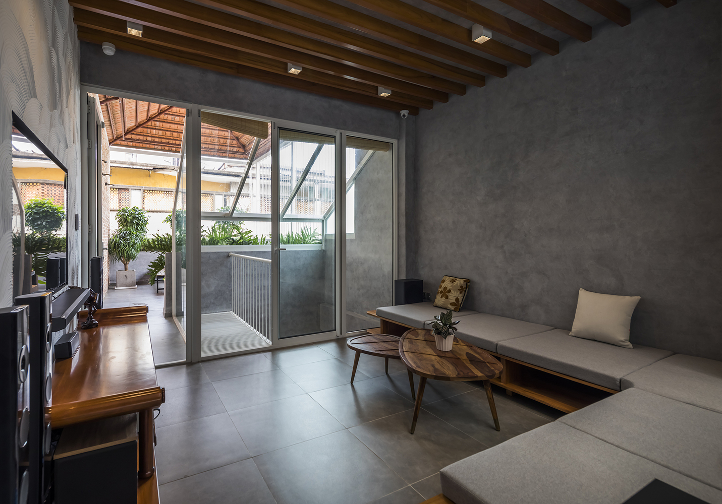 Không gian bên trong nhà ống Sài Gòn sau cải tạo phòng khách với tường bê tông, sofa ghi màu xám, bàn cà phê gỗ hình tam giác