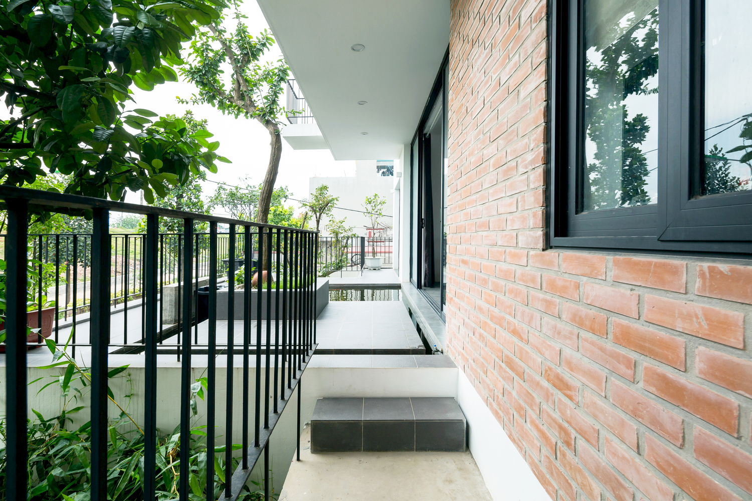 cận cảnh tường gạch đỏ, cửa sổ k&iacute;nh, lan can sắt, h&agrave;nh lang, c&acirc;y xanh
