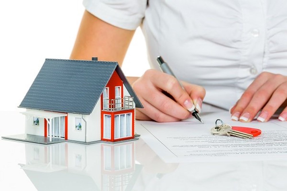 h&igrave;nh ảnh m&ocirc; h&igrave;nh ng&ocirc;i nh&agrave;, người mặc &aacute;o cộc tay m&agrave;u trắng đặt b&uacute;t k&yacute; v&agrave;o giấy tờ minh họa cho việc sang t&ecirc;n sổ đỏ