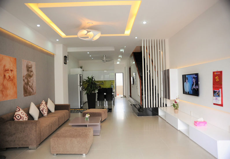 Ph&ograve;ng kh&aacute;ch nh&agrave; ống 3 tầng c&oacute; thiết kế hiện đại, tiết chế tối đa phụ kiện trang tr&iacute; nhằm tạo độ tho&aacute;ng cho căn  ph&ograve;ng. Lam gỗ sơn trắng kh&eacute;o l&eacute;o che chắn khu vực cầu thang.