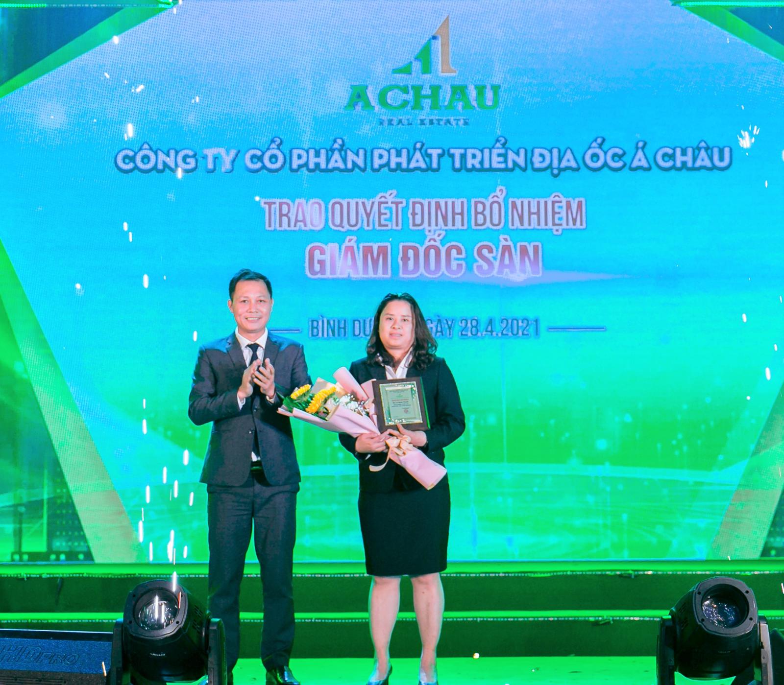 một người đ&agrave;n &ocirc;ng v&agrave; một người phụ nữ &ocirc;m hoa đứng tr&ecirc;n s&acirc;n khấu
