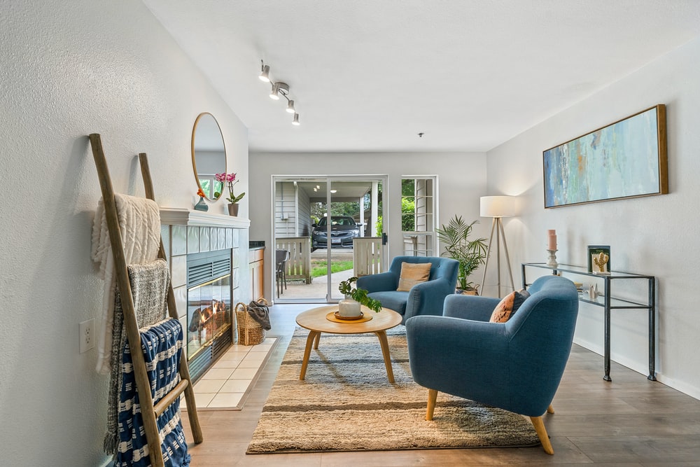 hình ảnh toàn cảnh phòng khách với sofa màu xanh dương, thang lưu trữ, gương tròn, cây xanh