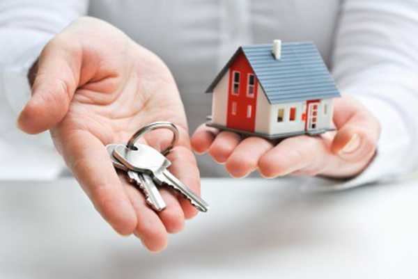 hình ảnh cận cảnh chìa khóa đặt trong lòng bàn tay, phía sau là bàn tay nâng đỡ mô hình ngôi nhà