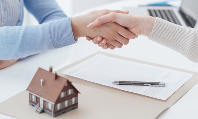 Đầu tư bất động sản cần lưu ý vị trí và pháp lý của tài sản hình ảnh bắt tay ký hợp đồng, phía dưới bàn là giấy tờ và mô hình ngôi nhà