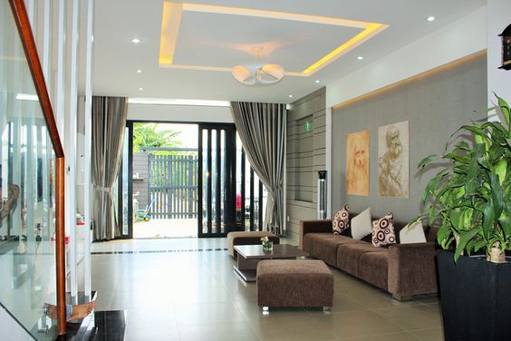 Phòng khách nhà ống thoáng rộng, ngập tràn ánh sáng tự nhiên nhờ hệ cửa kính cao rộng mở ra bên ngoài. Gia chủ kết hợp rèm che để đảm bảo tính riêng tư thiết yếu.