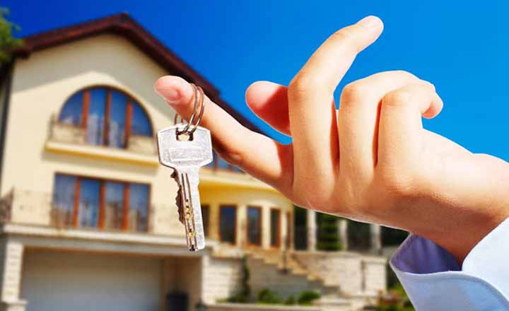 hình ảnh cận cảnh ngón tay treo chìa khóa, xa xa là hình ảnh ngôi nhà