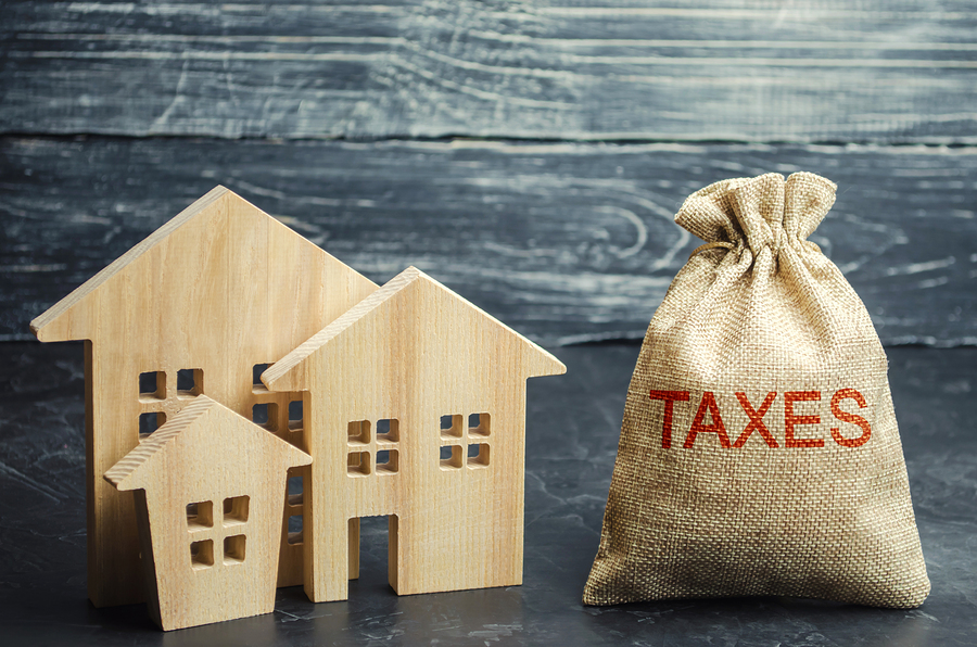 3 mô hình ngôi nhà bằng gỗ, cạnh đó là túi gai ghi chữ taxes