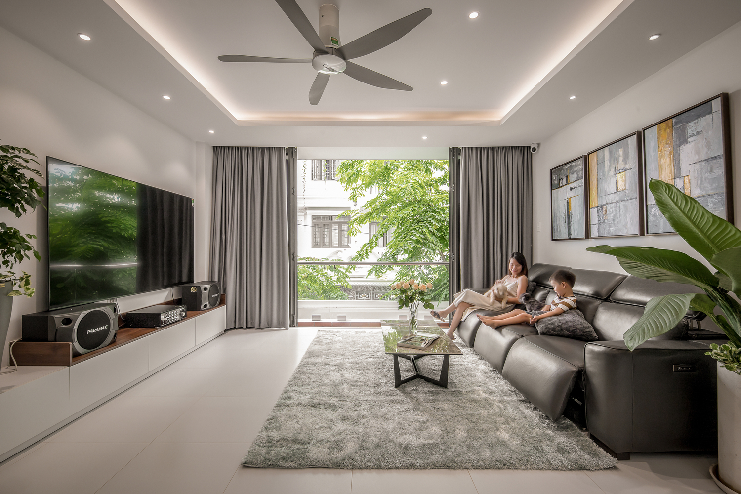 Phòng khách nhà phố rộng thoáng, nhiều ánh sáng tự nhiên. hai mẹ con ngồi trên sofa phòng khách nhà phố rộng thoáng