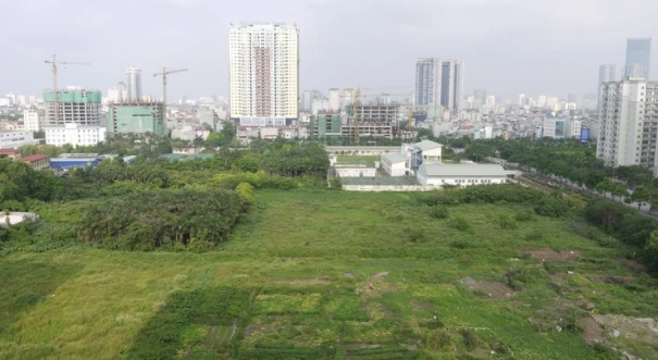 H&igrave;nh ảnh khu đất trống cỏ mọc xanh tốt cạnh c&aacute;c t&ograve;a nh&agrave; cao tầng, đ&ocirc; thị minh họa cho việc thu hồi đất