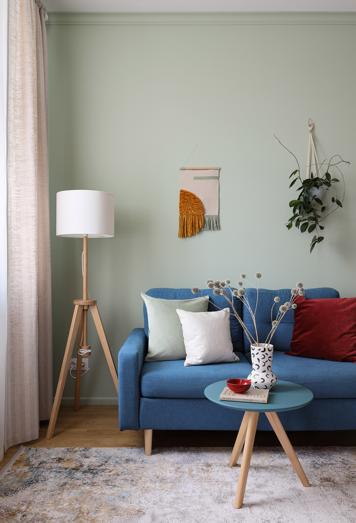 G&oacute;c ph&ograve;ng kh&aacute;ch với sofa xanh, đ&egrave;n s&agrave;n m&agrave;u trắng, r&egrave;m cửa, chậu c&acirc;y treo tường