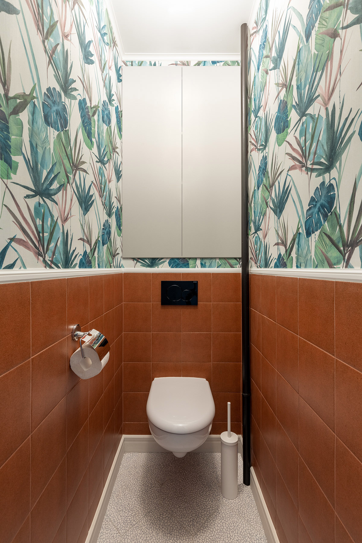 WC nhỏ xinh với gạch ốp t&ocirc;ng m&agrave;u đất th&acirc;n thiện, phần tường ph&iacute;a tr&ecirc;n trang tr&iacute; giấy d&aacute;n tường họa tiết nhiệt đới xanh m&aacute;t.
