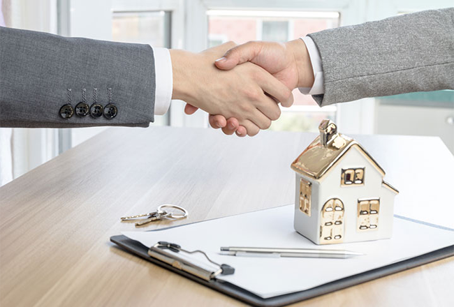 hình ảnh bắt tay minh họa cho chuyển nhượng bất động sản, phía dưới là mô hình ngôi nhà đặt trên giấy tờ tài liệu