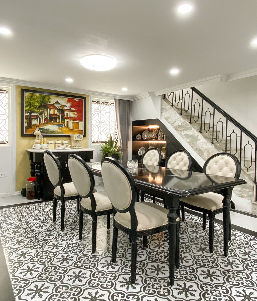 Ph&ograve;ng ăn được định vị bởi khoảng s&agrave;n l&aacute;t gạch b&ocirc;ng họa tiết cổ điển bắt mắt. Khoảng trống gầm cầu thang được tận dụng kh&eacute;o l&eacute;o l&agrave;m nơi trưng b&agrave;y đồ gốm.