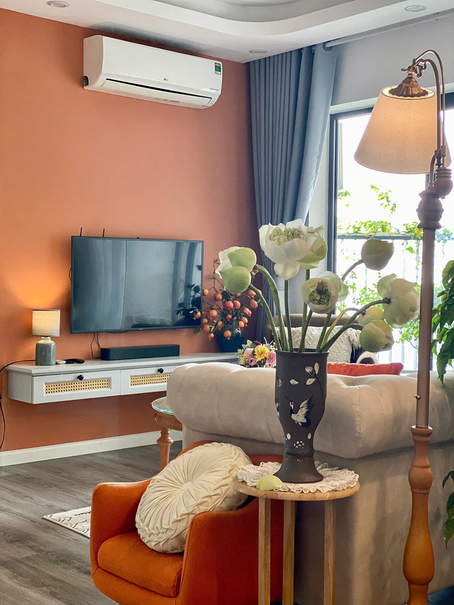 G&oacute;c ph&ograve;ng kh&aacute;ch với tường sau tivi sơn m&agrave;u cam, ghế b&agrave;nh m&agrave;u cam, b&igrave;nh hoa sen 