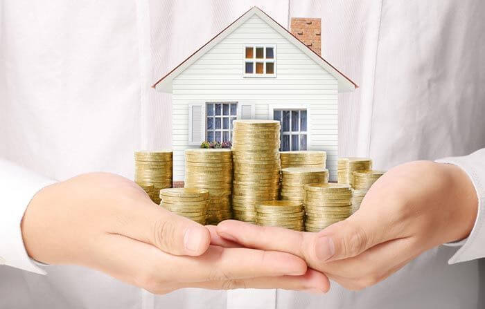 Bán nhà chung cư phải đóng thuế, phí gì? hình ảnh một người mặc sơ mi trắng ôm mô hình ngôi nhà và các cọc tiền xu minh họa cho việc bán nhà chung cư