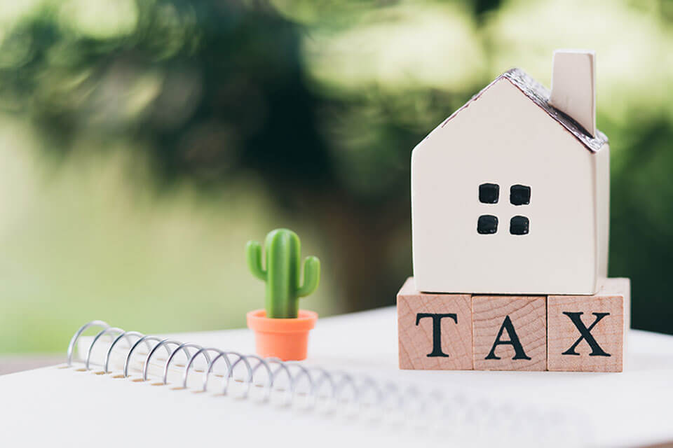 h&igrave;nh ảnh minh họa cho thuế b&aacute;n nh&agrave; với chữ TAX lớn ph&iacute;a tr&ecirc;n l&agrave; m&ocirc; h&igrave;nh ng&ocirc;i nh&agrave;