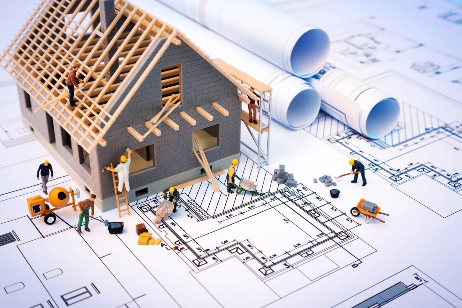 mô hình ngôi nhà đang được xây dựng nằm trên bản vẽ thiết kế