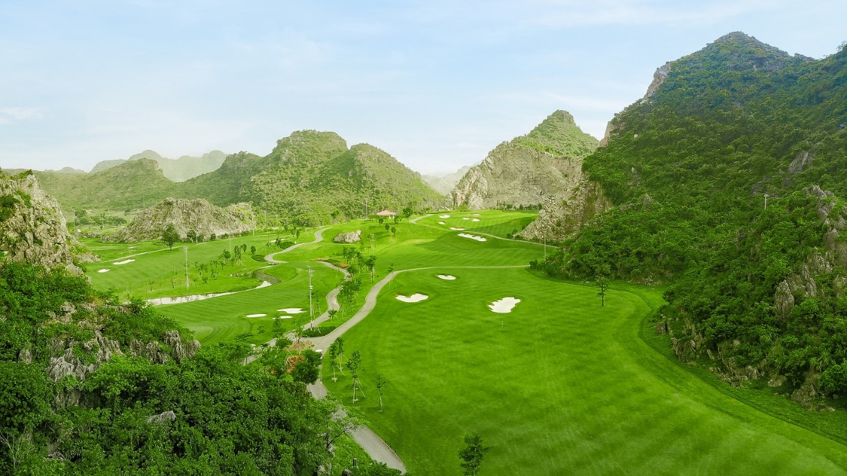 Legend Valley Country Club: Từ vùng đầm lầy hoang sơ đến 'thiên đường golf' giữa lòng Ninh Bình- Ảnh 2. A golf course with a path and mountains AI-generated content may be incorrect.