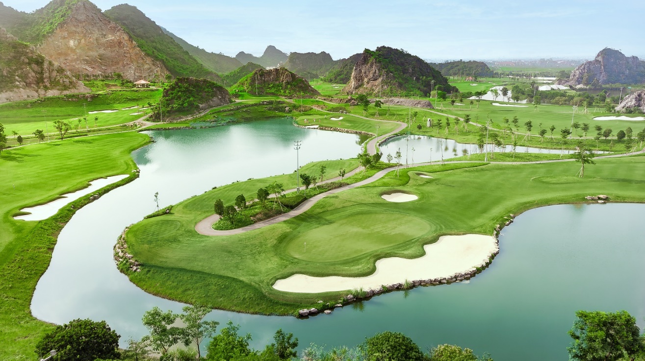 Legend Valley Country Club: Từ vùng đầm lầy hoang sơ đến 'thiên đường golf' giữa lòng Ninh Bình- Ảnh 4. A golf course with a lake and mountains AI-generated content may be incorrect.