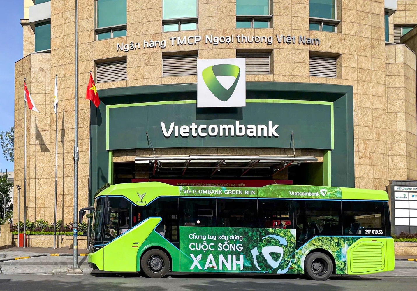Ngân hàng có 24.000 nhân sự chính thức vận hành buýt điện đưa đón nhân viên: Khi ESG không nằm trên giấy- Ảnh 1. A green bus parked in front of a building AI-generated content may be incorrect.