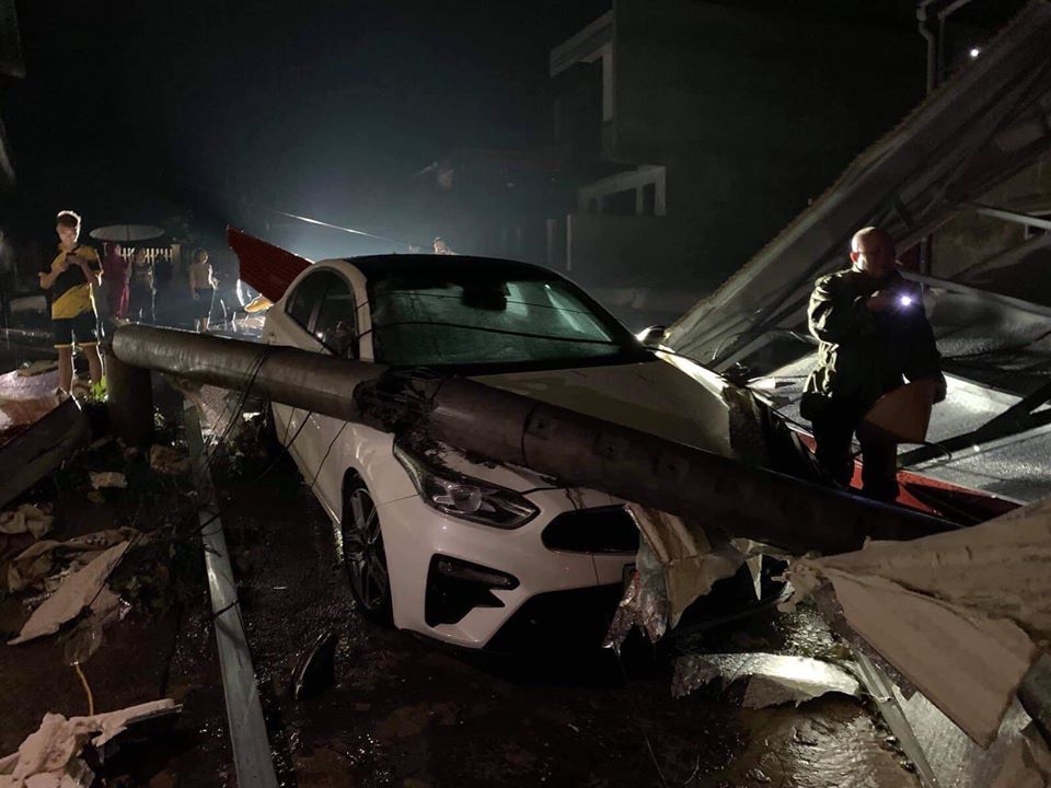 Một trụ điện đổ xuống v&agrave; đ&egrave; tr&uacute;ng một chiếc xe Kia Cerato 2019 m&agrave;u trắng khiến xe hư hỏng.