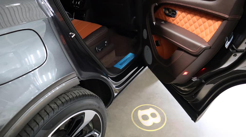 Logo Bentley với nền màu vàng phản chiếu dưới nền gạch khi mở cửa xe