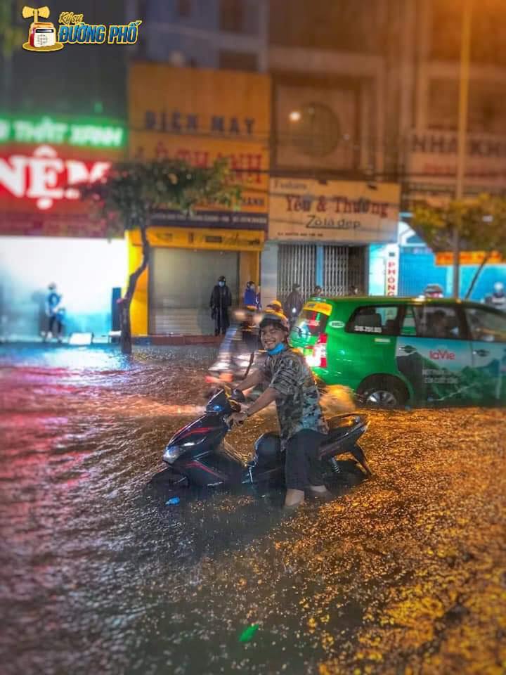 Nụ cười của một thanh niên dắt xe máy trên đường ngập Nụ cười của một thanh niên dắt xe máy trên đường ngập
