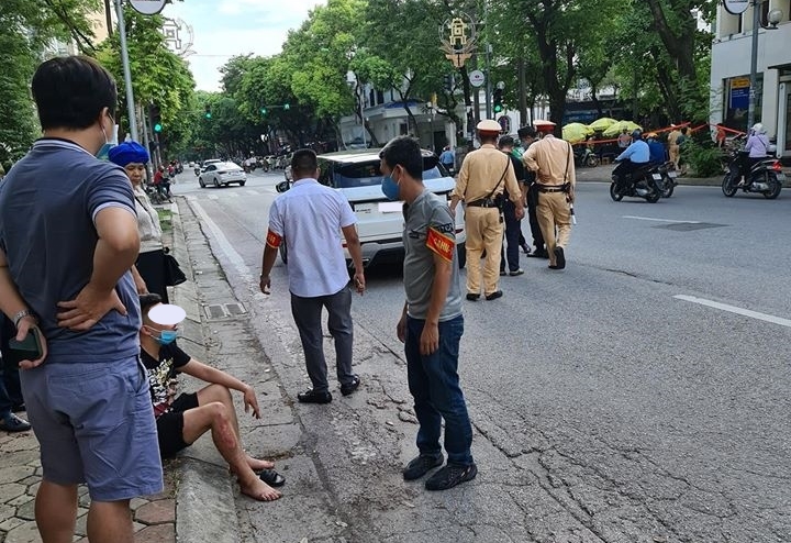 Nam thanh niên chạy xe máy ngồi bên lề đường trong khi lực lượng chức năng đang giải quyết vụ va chạm giao thông