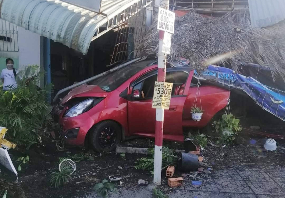 Chiếc xe Chevrolet Spark hư hỏng đầu xe, quán cà phê bên đường và mái hiên nhà dân hư hỏng nặng Chiếc xe Chevrolet Spark hư hỏng đầu xe, quán cà phê bên đường và mái hiên nhà dân hư hỏng nặng