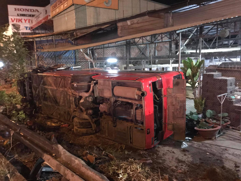 Chiếc xe khách sau tai nạn với xe tải đã tông vào dải ta-luy bên đường rồi lật nghiêng trước một trại hòm Chiếc xe khách sau tai nạn với xe tải đã tông vào dải ta-luy bên đường rồi lật nghiêng trước một trại hòm